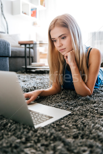 Stock photo: Beautiful young woman lying and using laptop on carpet