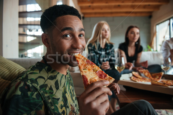 Man eating slice of pizza while hanging out with friends Stock photo © deandrobot