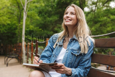 Smiling young brunette girl sitting on bench with laptop computer Stock photo © deandrobot