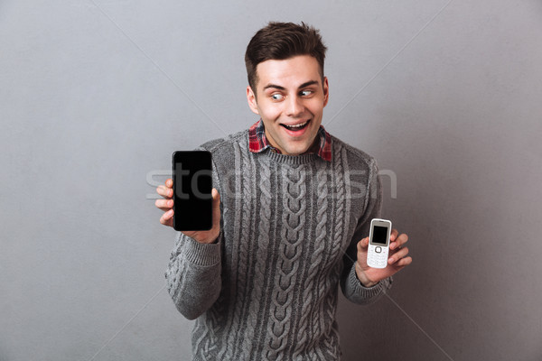 Intrigued man in sweater choosing between smartphones Stock photo © deandrobot
