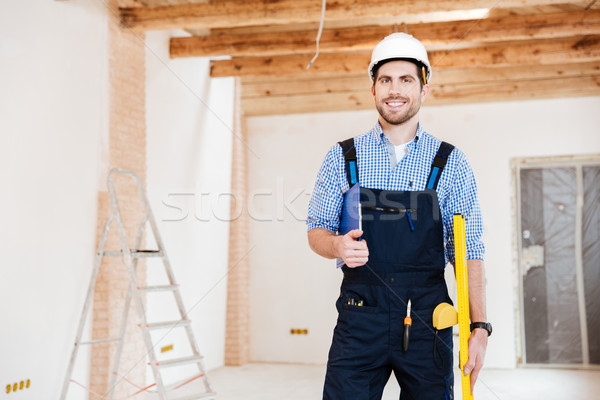 Young handsome builder standing and smiling at the working place Stock photo © deandrobot