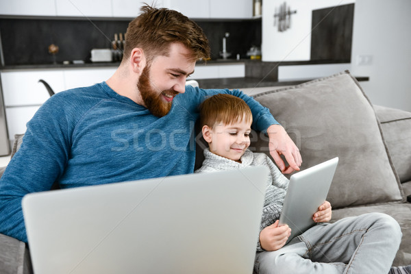 Happy father using laptop while his son look at tablet Stock photo © deandrobot