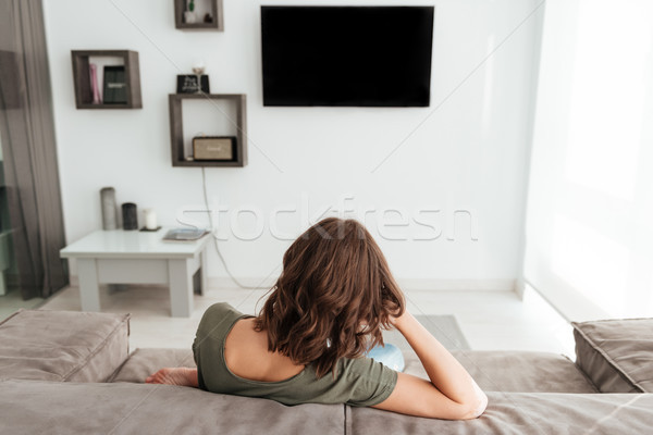 Back view of woman sitting on sofa and watching TV Stock photo © deandrobot