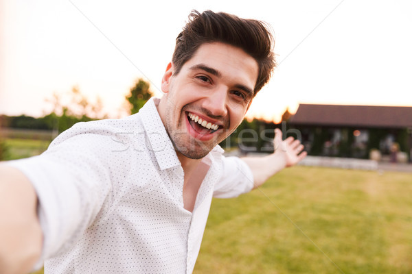 Image of happy adult man wearing white shirt laughing, while tak Stock photo © deandrobot