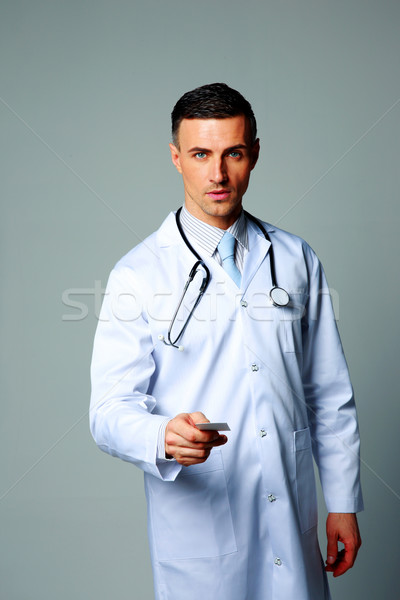 Stock photo: Confident male doctor giving card on gray background