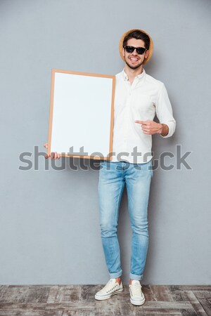 Happy man in sunglasses standing and holding blank white board Stock photo © deandrobot