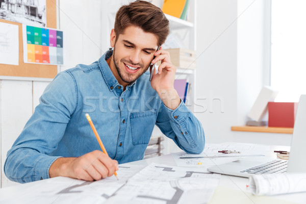 Smiling young businessman talking on mobile phone and making notes Stock photo © deandrobot