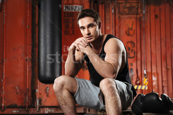 Young man sitting in a gym near boxing gloves Stock photo © deandrobot