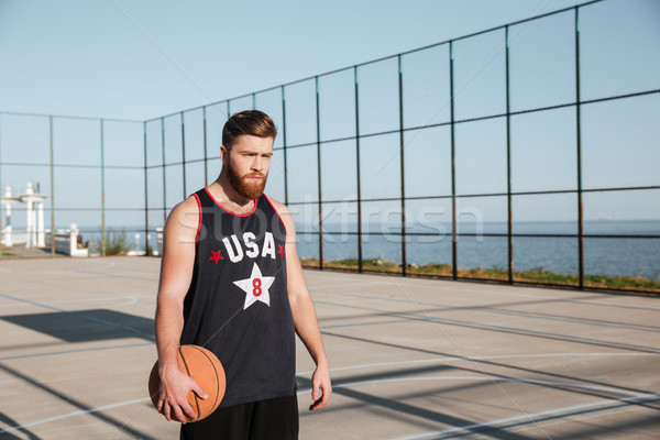 Concentrated bearded sportsman holding basketball while standing on playground Stock photo © deandrobot