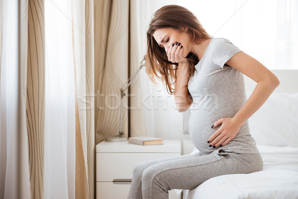 Terhes fiatal nő ül ágy érzés beteg Stock fotó © deandrobot