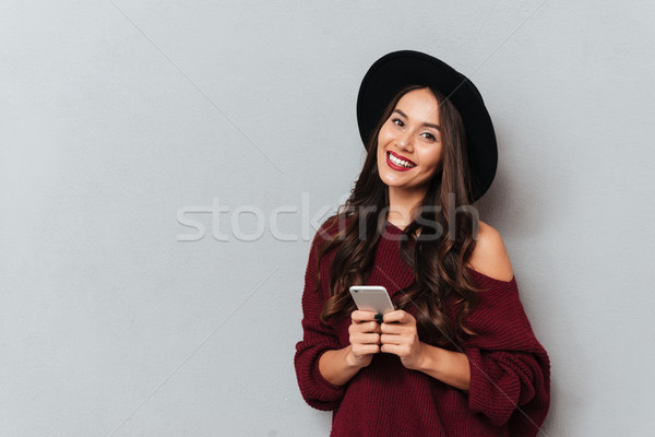 Beautiful smiling brunette woman in black hat holding mobile pho Stock photo © deandrobot