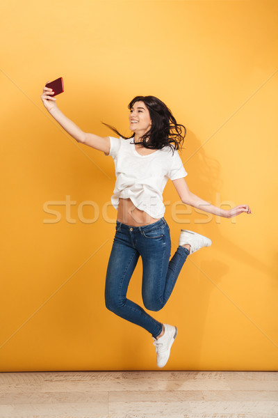 Emotional woman jumping make selfie by mobile phone. Stock photo © deandrobot