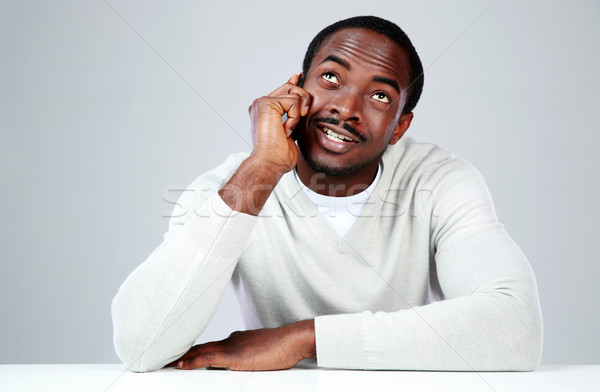 Smiling african man sitting at the table and talking on the phone over gray background Stock photo © deandrobot