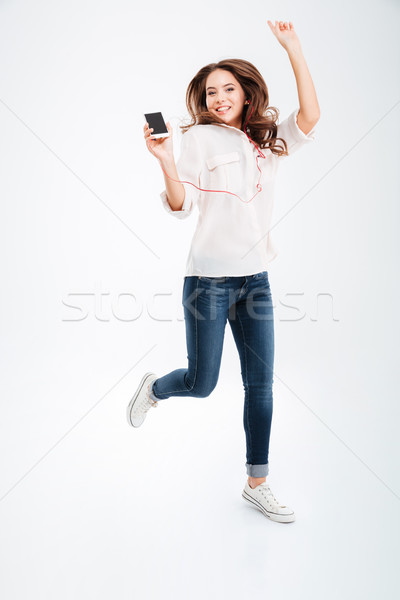 Full length portrait of a woman listening music and jumping Stock photo © deandrobot