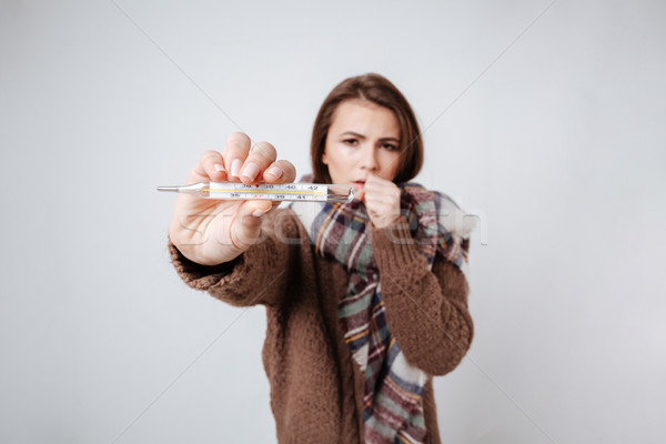 Stock photo: Sick woman in sweater and scarf showing thermometer