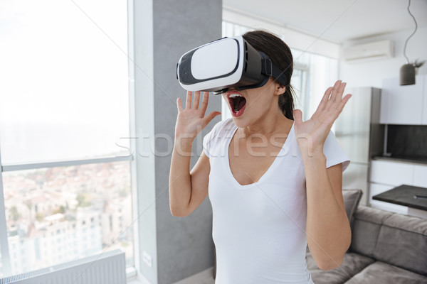 Amazed happy young woman using virtual reality googles at home Stock photo © deandrobot