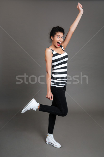Happy excited african woman standing with raised hand and shouting Stock photo © deandrobot
