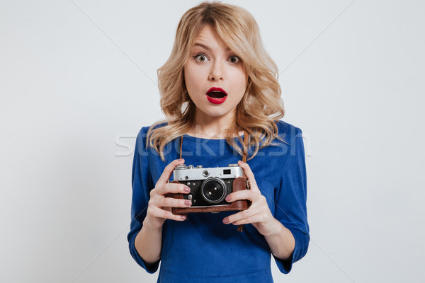 Shocked young lady holding camera over white background. Stock photo © deandrobot