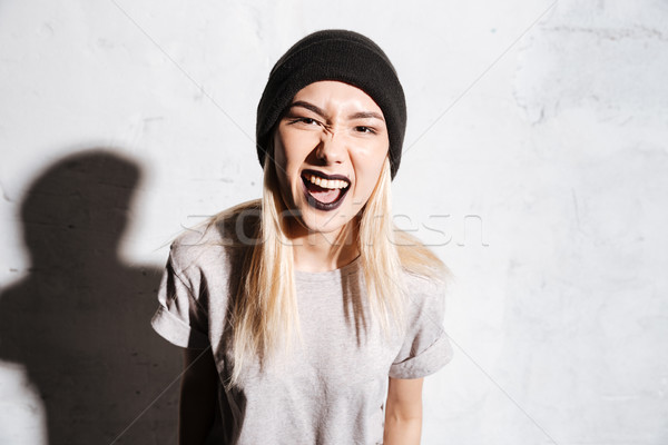 Angry irritated young woman in black hat standing and screaming Stock photo © deandrobot
