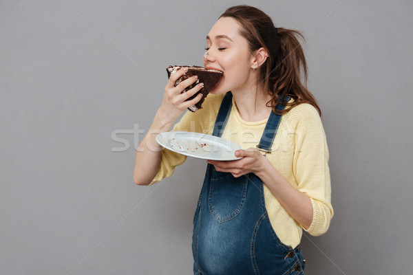 Portrait of a happy cute pregnant woman biting chocolate cake Stock photo © deandrobot