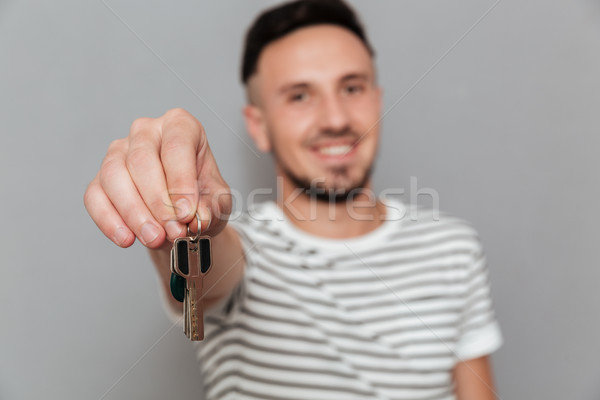 Smiling man in t-shirt showing keys at the camera Stock photo © deandrobot