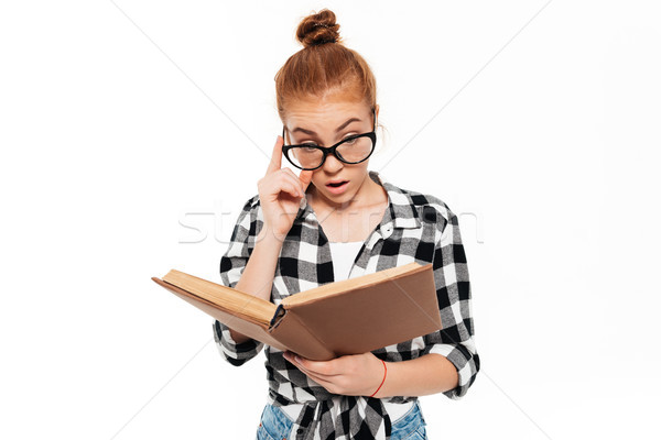 Surprised ginger woman in shirt and eyeglasses reading book Stock photo © deandrobot