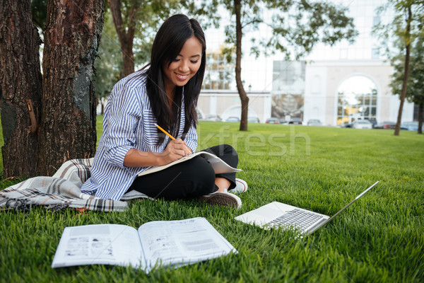 Beautiful asian student keeping records in paper notebook while  Stock photo © deandrobot