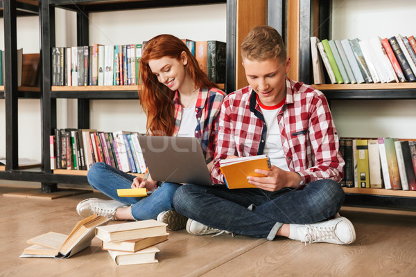 Smiling teenage couple sitting on a floor at the bookshelf Stock photo © deandrobot
