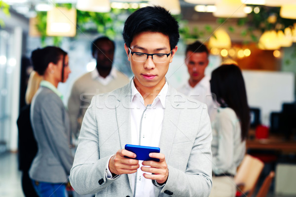 Asian businessman using smartphone in front of colleagues Stock photo © deandrobot