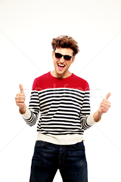 Laughing young man in sunglasses with thumbs up over white background Stock photo © deandrobot