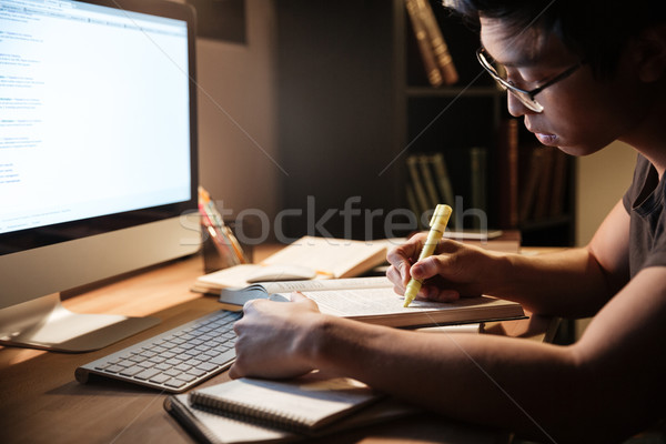 Serious man studying with books and computer in dark room  Stock photo © deandrobot