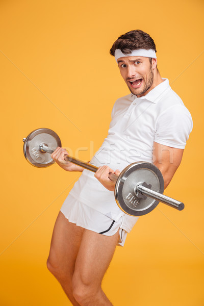 Amusing young sportsman shouting and holding heavy barbell Stock photo © deandrobot