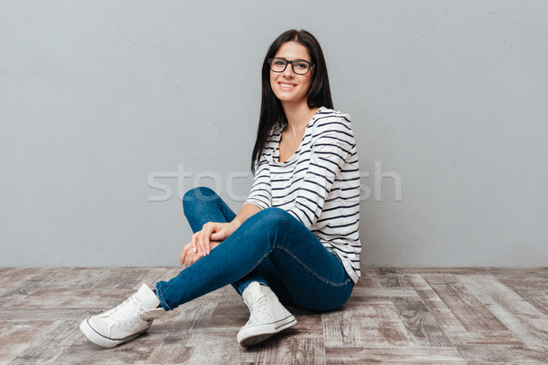 Happy young woman sitting on floor over grey background Stock photo © deandrobot