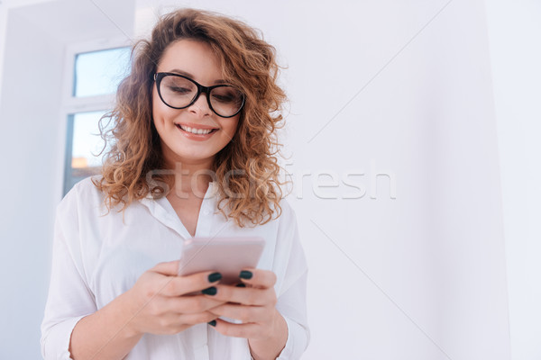 Smiling Woman in shirt writing message on phone Stock photo © deandrobot