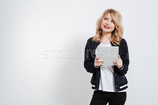 Young woman in casual clothes thinking and holding tablet computer Stock photo © deandrobot