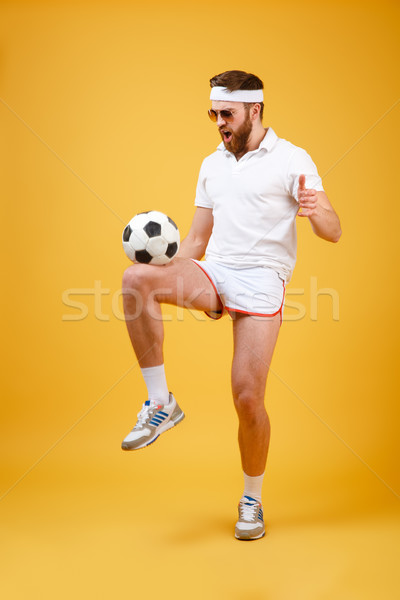 Handsome emotional young sportsman make football exercises with ball Stock photo © deandrobot