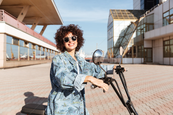 Vedere laterala zâmbitor fată ochelari de soare prezinta motocicletă Imagine de stoc © deandrobot