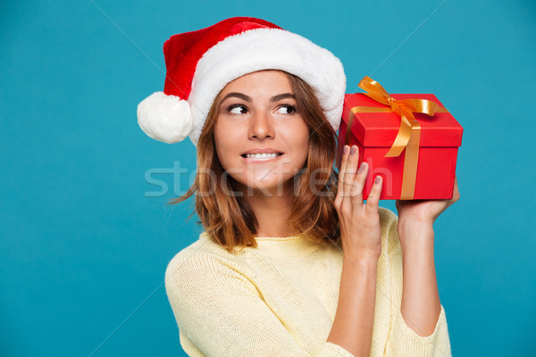 Pleased intrigued woman in sweater and christmas hat holding gift Stock photo © deandrobot