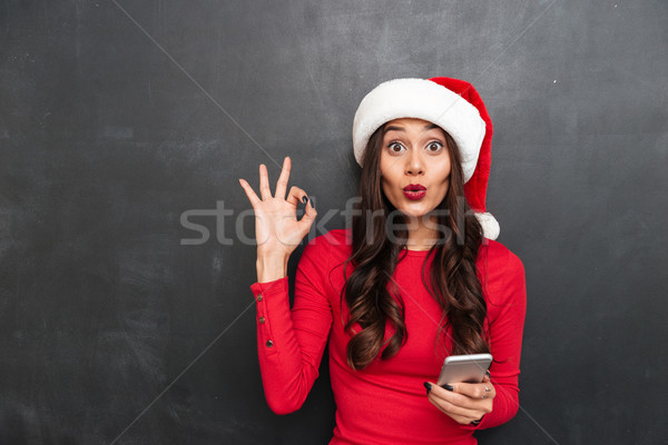 Surprised brunette woman in red blouse and christmas hat Stock photo © deandrobot