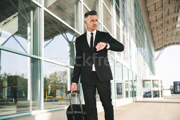 Nyugodt üzletember öltöny sétál bőrönd kívül Stock fotó © deandrobot