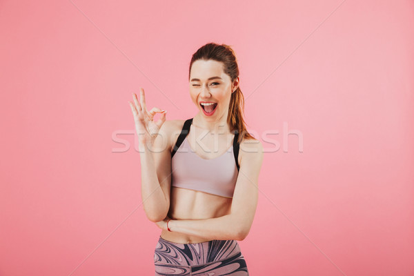 Cheerful sportswoman showing ok sign while winks with eye Stock photo © deandrobot