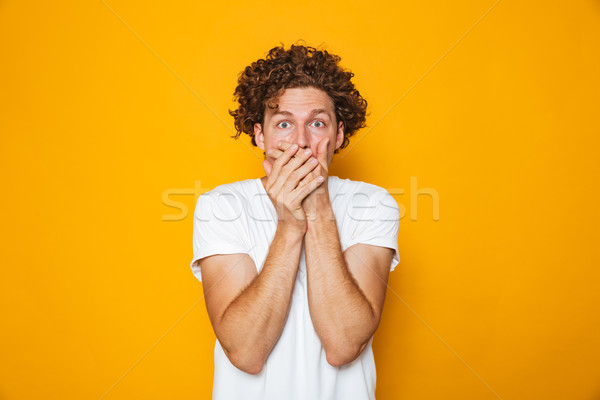 Portrait of a shocked curly haired man covering mouth Stock photo © deandrobot