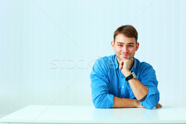 Young happy businessman in blue shirt sitting at the table in office Stock photo © deandrobot