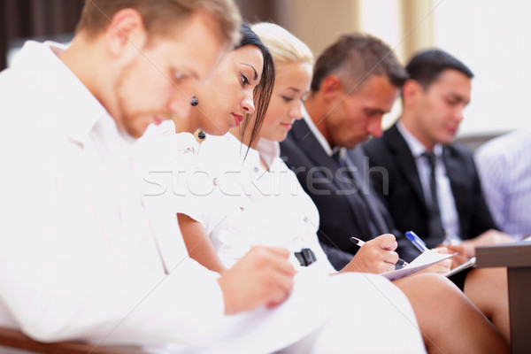 Business people sitting in a row at meeting and making notes. Focus on woman Stock photo © deandrobot