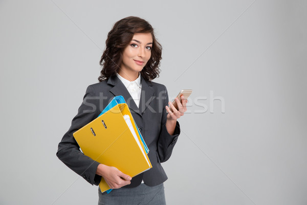 Pretty young business woman using cellphone and holding binders Stock photo © deandrobot