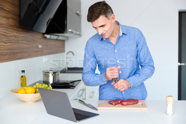 Handsome male watching cooking lesson on laptop and preparing me Stock photo © deandrobot