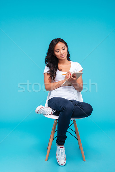 Pensive concentrated young asian woman making notes in notebook Stock photo © deandrobot