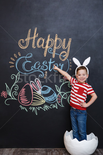 Happy little boy wearing rabbit ears and standing inside big cracked eggshell Stock photo © deandrobot