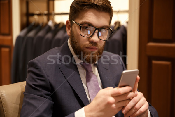 Concentrated young bearded businessman sitting indoors chatting Stock photo © deandrobot