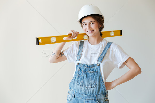 Stock photo: Young smiling woman in hardhat holding yellow level tool